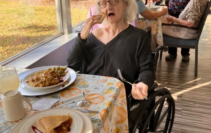 An elderly woman in a wheelchair enjoying a meal indoors.