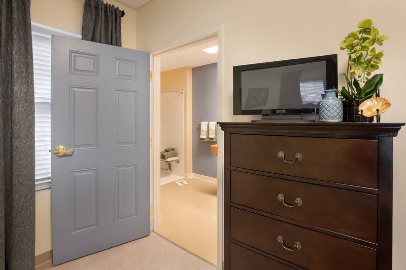 A bedroom with a dresser and television, leading to a bathroom.