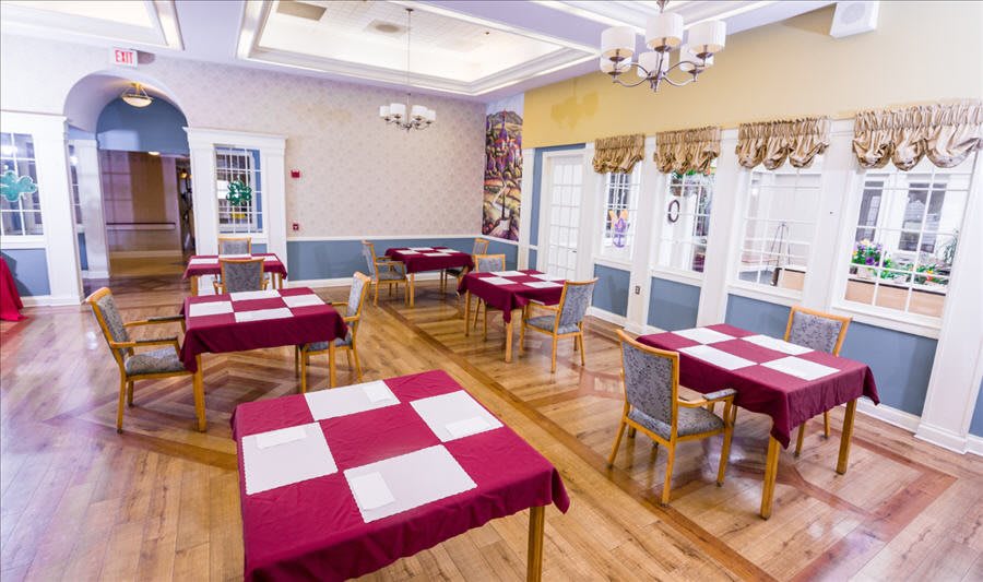 A brightly lit dining room with red and white checkered tablecloths, arranged neatly with chairs around wooden tables.