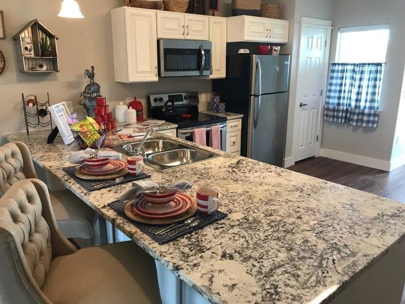 A modern kitchen featuring a granite countertop with place settings, a microwave, and a refrigerator.