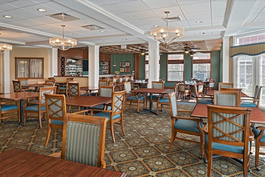 A spacious dining area with elegant furnishings, including wooden tables and chairs, chandeliers, and a patterned carpet.