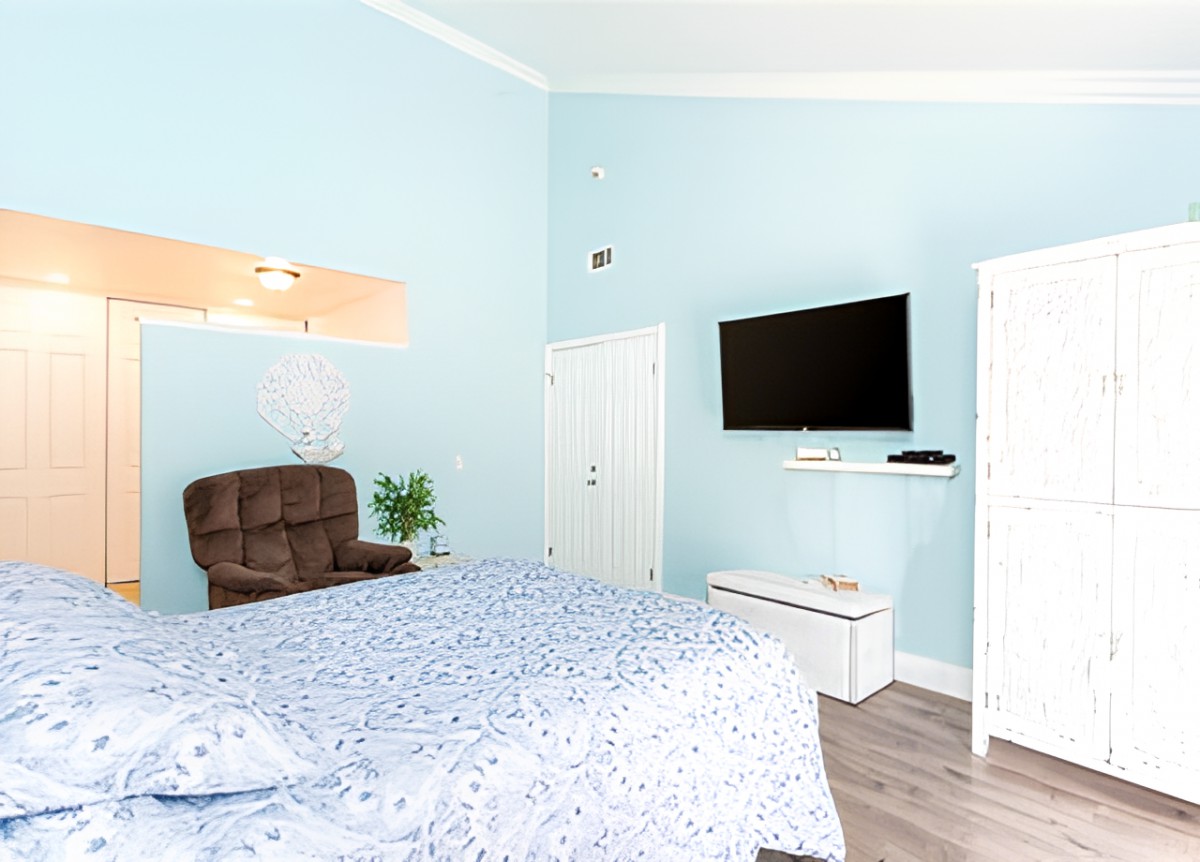 A modern bedroom with blue walls featuring a bed, wall-mounted TV, and comfortable armchair.