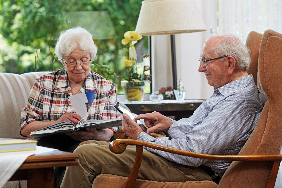 An elderly couple sitting together in a living room, engaged in reading and relaxing.