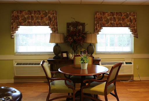 A cozy dining area featuring a round table and comfortable chairs, adorned with decorative curtains and a floral arrangement.