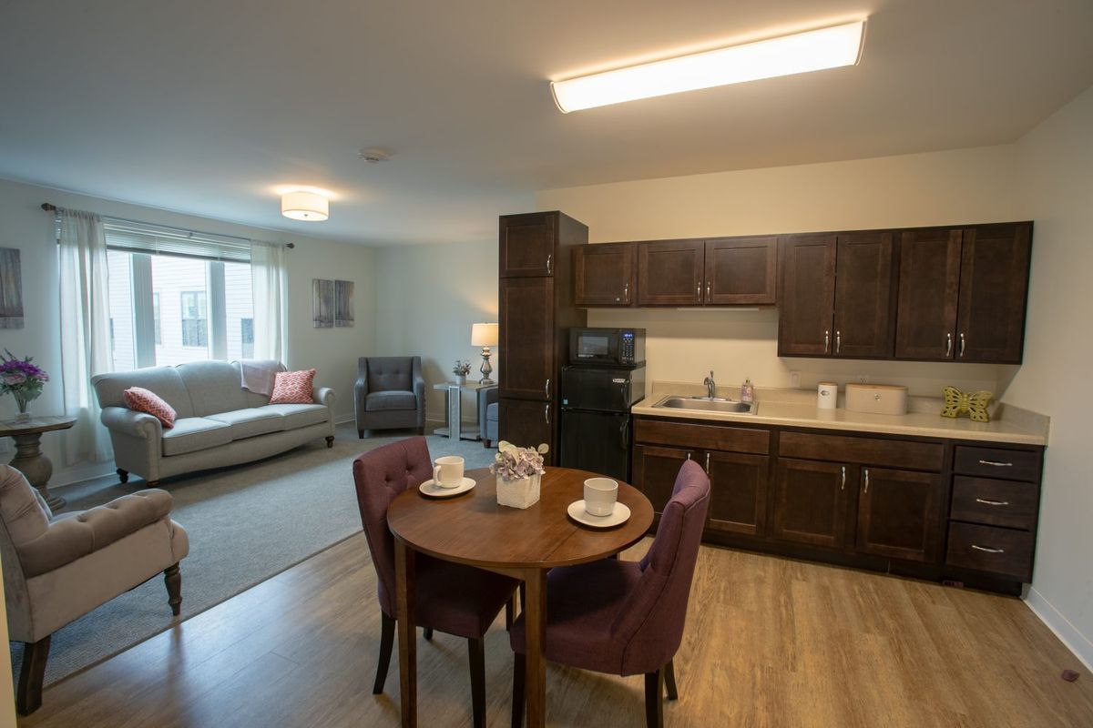 A cozy apartment interior with a combined living room and kitchen, featuring a dining table with two chairs.