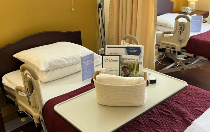 A hospital room with a neatly made bed, adorned with linens and informational pamphlets on a tray table.