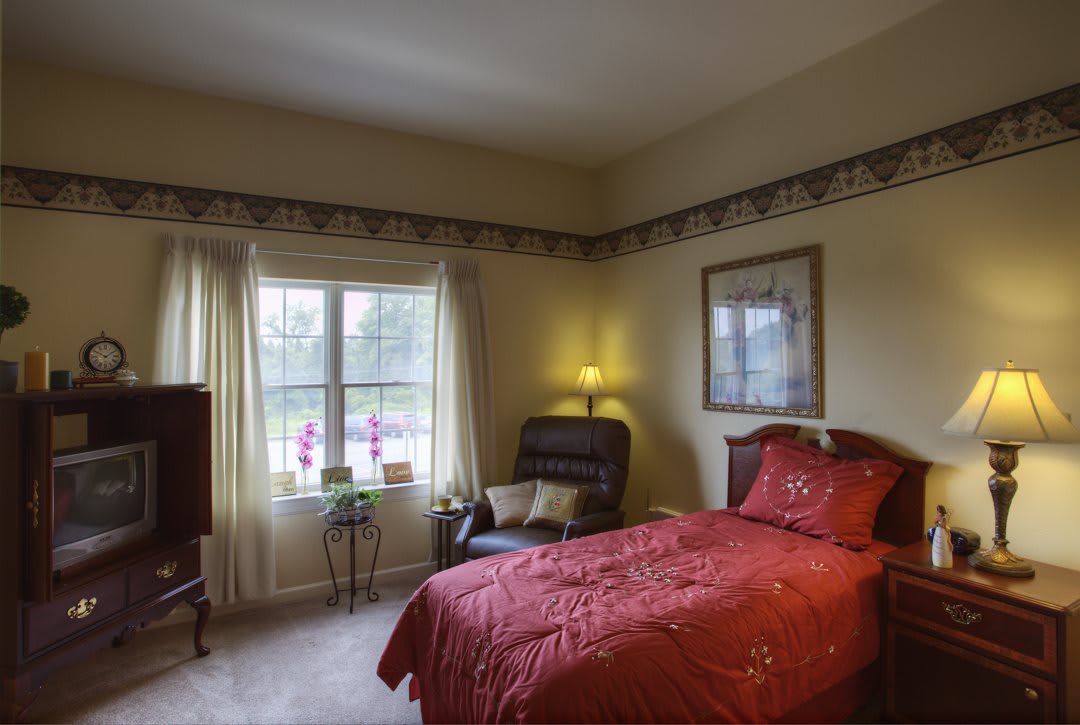 A cozy bedroom with a single bed, soft lighting, and a view of the garden through the window.