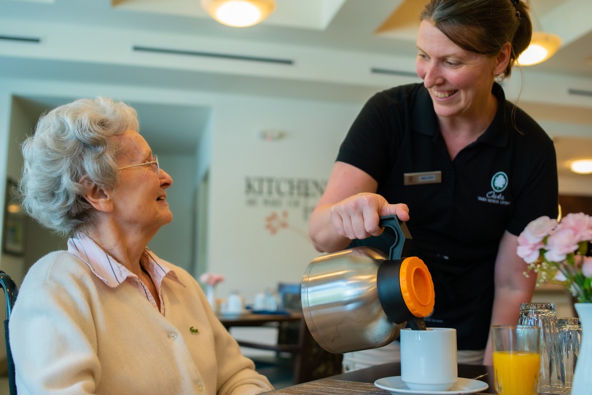 A caregiver pouring tea for an elderly woman, showcasing warmth and care.