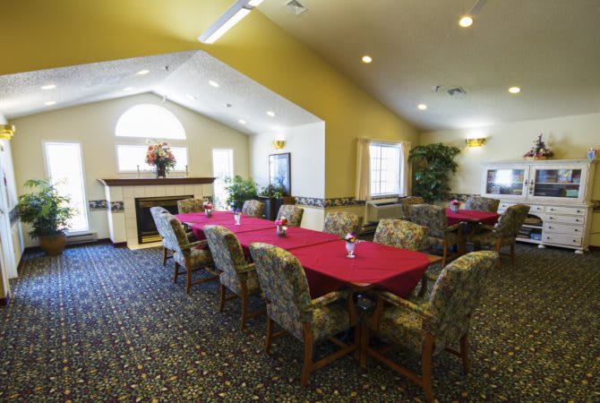 A well-lit dining room with neatly arranged tables and chairs, featuring a fireplace and decorative plants.