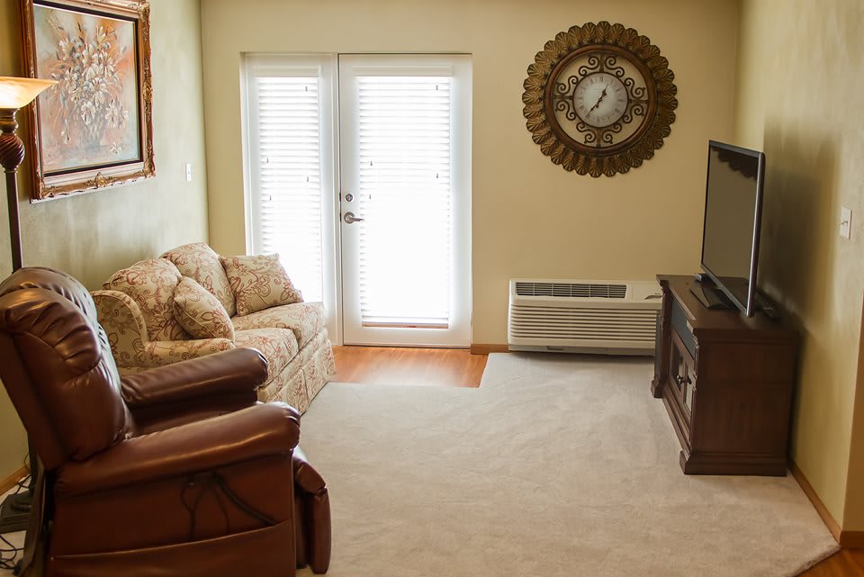 A cozy living room with a sofa, armchair, television, and wall clock.