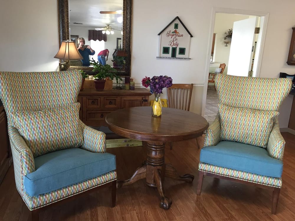A cozy living room setup featuring two comfortable chairs and a round wooden table adorned with a vase of purple flowers.