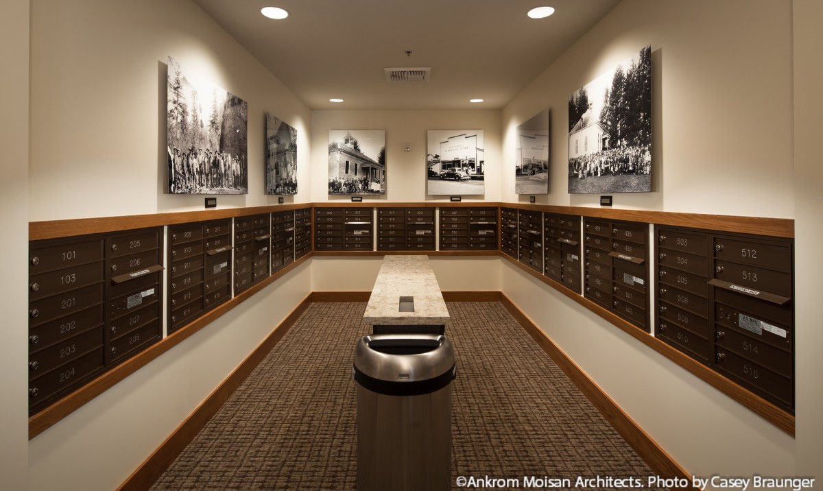 A well-designed mailroom featuring black and white photographs on the walls, with organized mailboxes and a central bench.