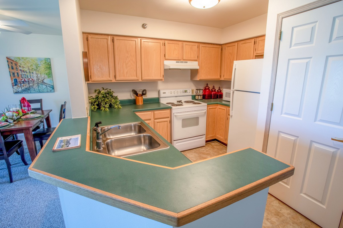 A cozy kitchen with green countertops and wooden cabinets, featuring standard appliances.