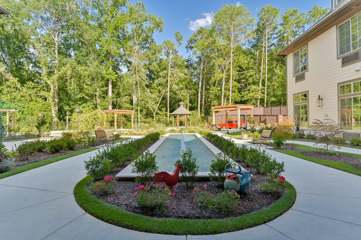 A beautifully landscaped garden with a central pool surrounded by colorful flowers and trees, creating a serene outdoor space.
