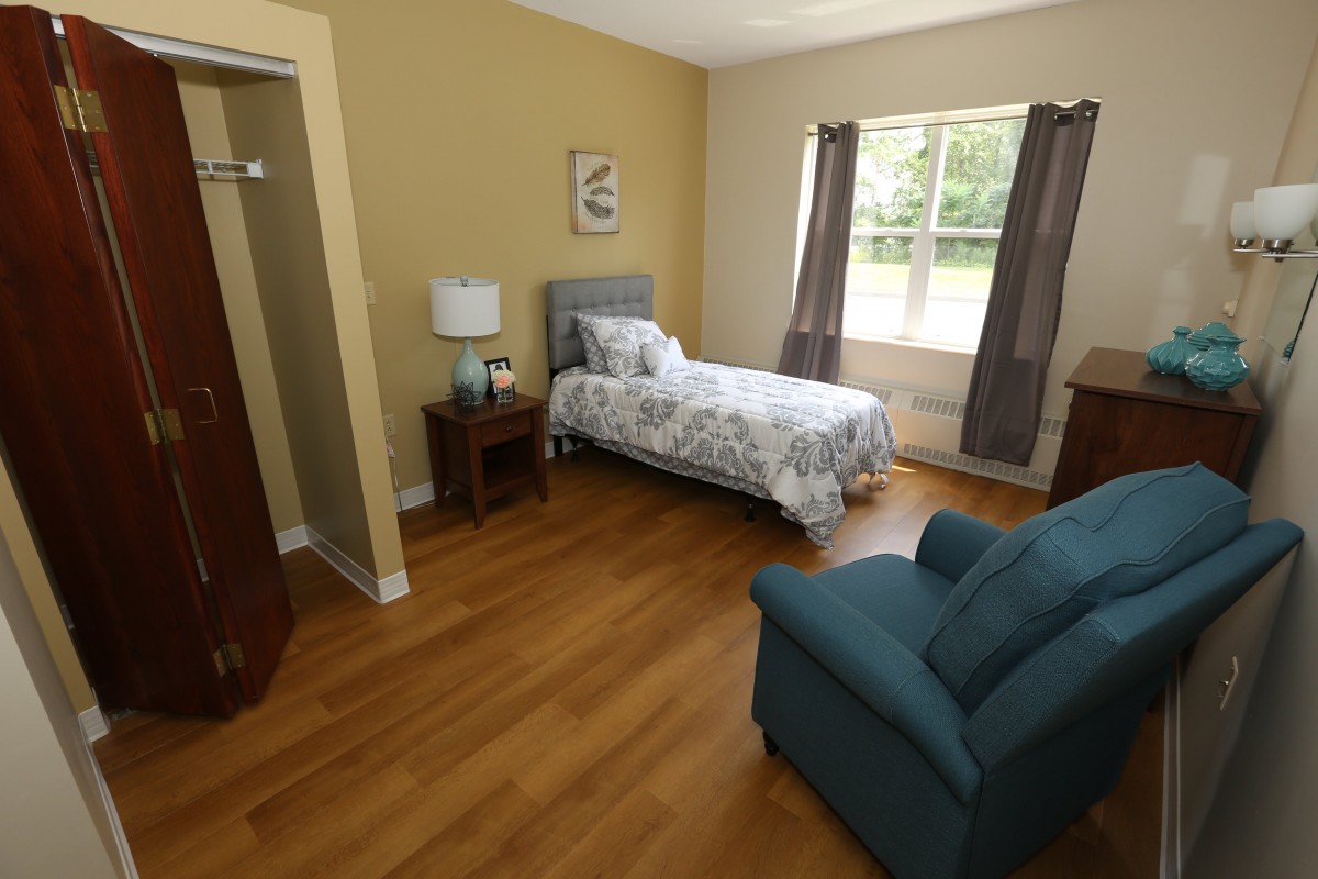 A cozy bedroom with a single bed, armchair, and wooden flooring.