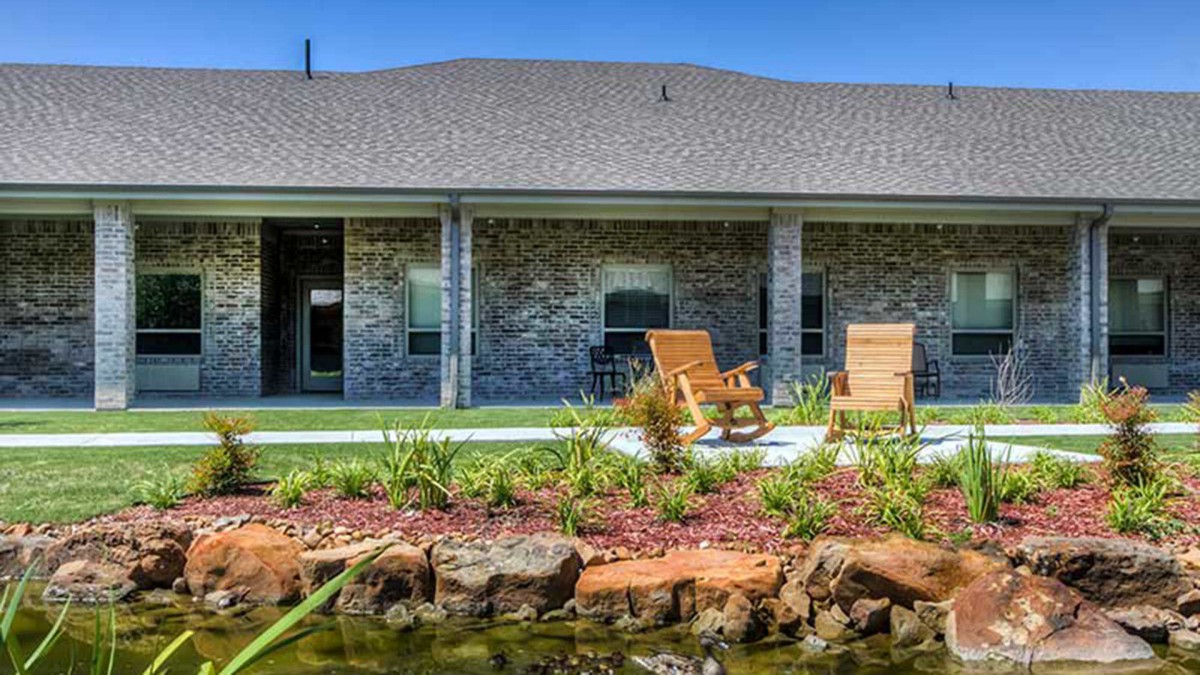 A cozy backyard patio with wooden rocking chairs and a landscaped garden.