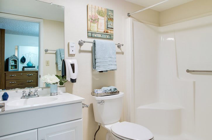 A clean and neatly organized bathroom with a shower, toilet, sink, mirror, and light blue towels.