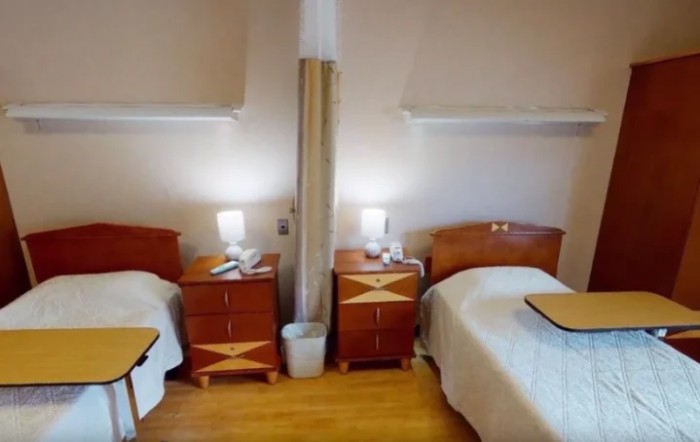 A hospital room featuring two beds separated by a curtain, each with a nightstand and lamp.