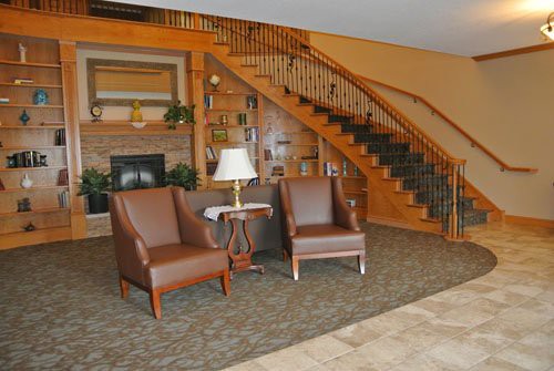 A cozy lobby area featuring two leather chairs, a small table with a lamp, and a wooden staircase.