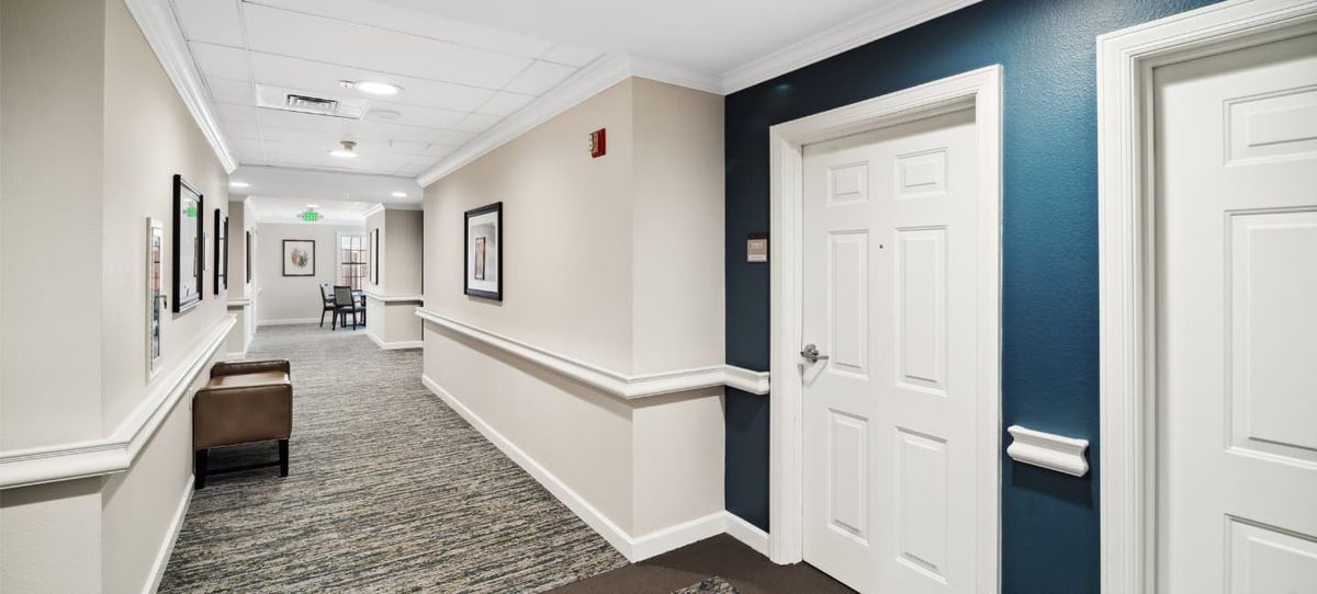 A well-lit hallway with a carpeted floor, featuring a closed door and framed artwork on the wall.