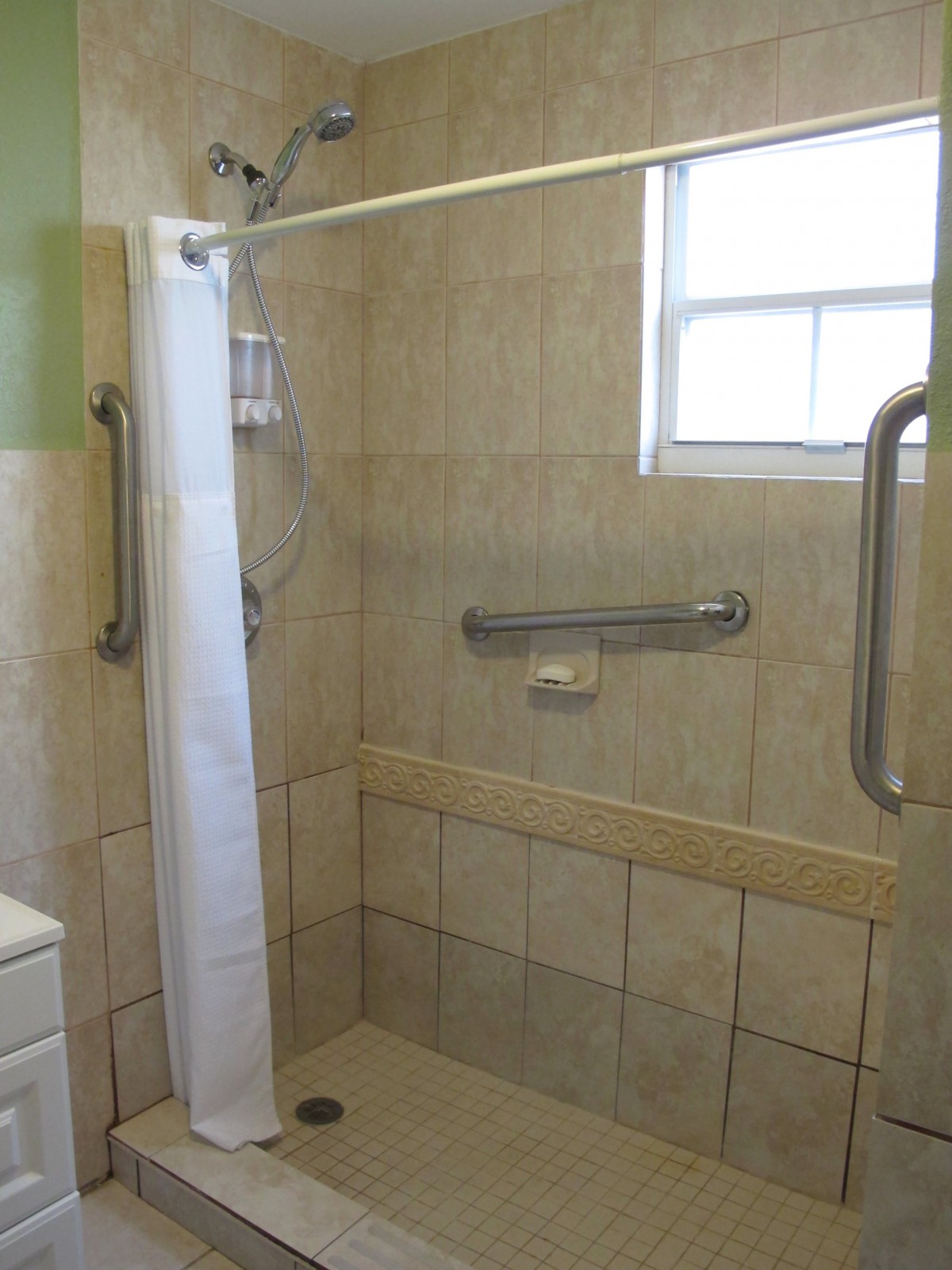 A bathroom shower area with grab bars and a tiled wall.