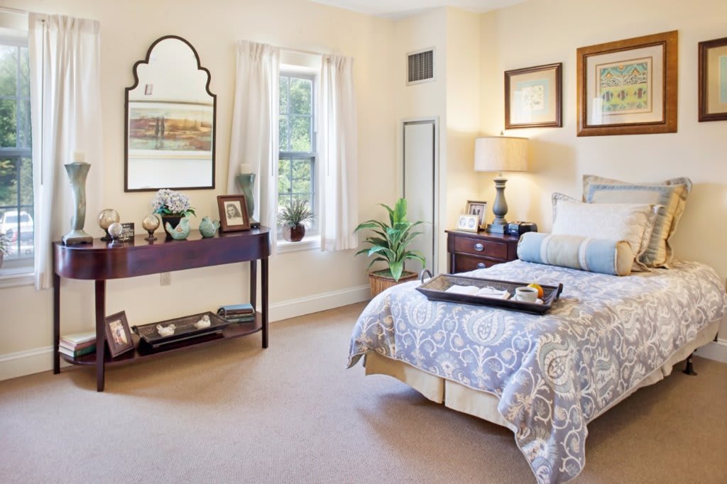 A well-decorated bedroom featuring a cozy bed, elegant furnishings, a wall mirror, and indoor plants.