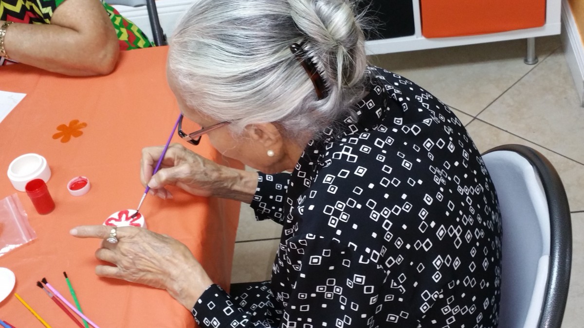 An elderly woman is focused on writing at a table indoors.