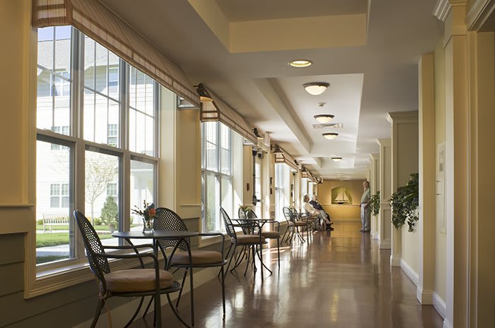 A well-lit hallway with chairs lined up along large windows, creating a welcoming seating area.