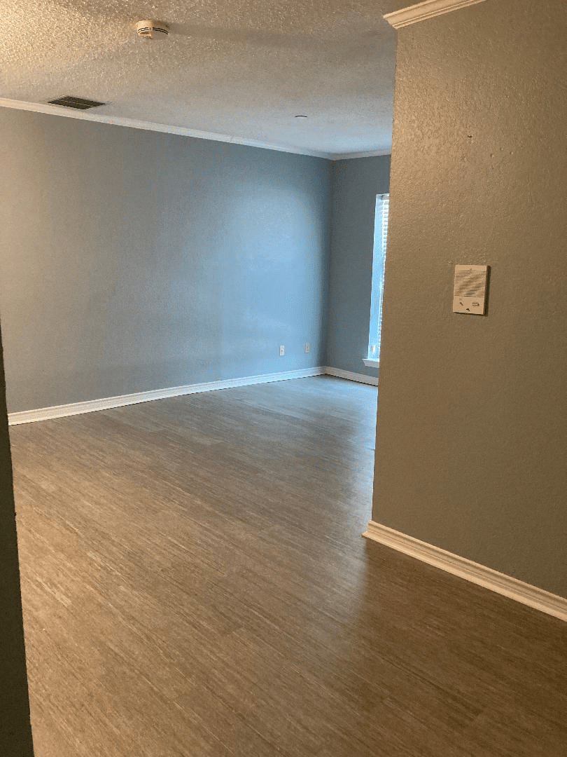 An empty room with grey walls and wood flooring, illuminated by natural light from a window.