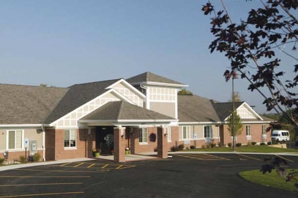 A brick building with a gabled roof and landscaped entrance under a clear sky.