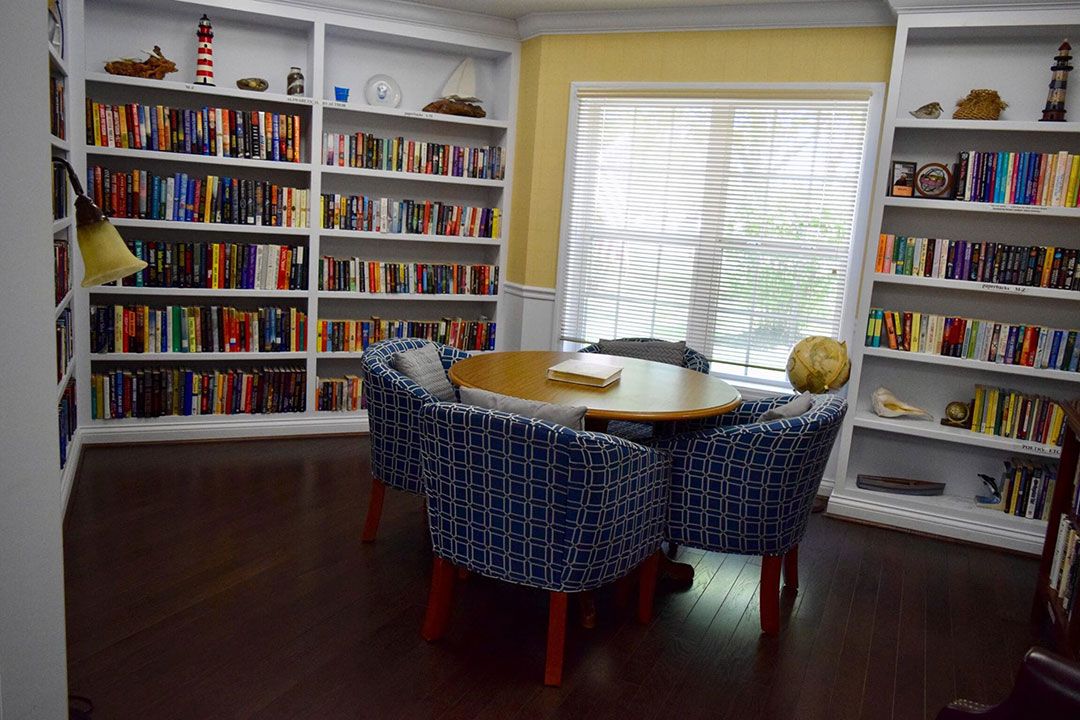 A cozy library corner with bookshelves and a round table surrounded by chairs.