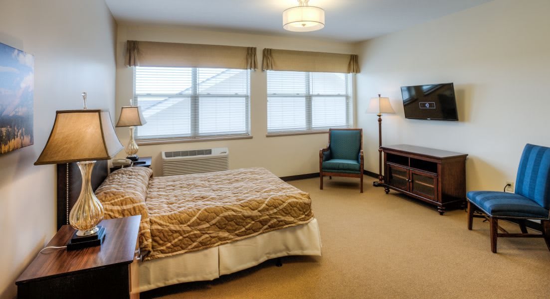 A neatly arranged hotel bedroom featuring a bed, windows, lamps, and a television.