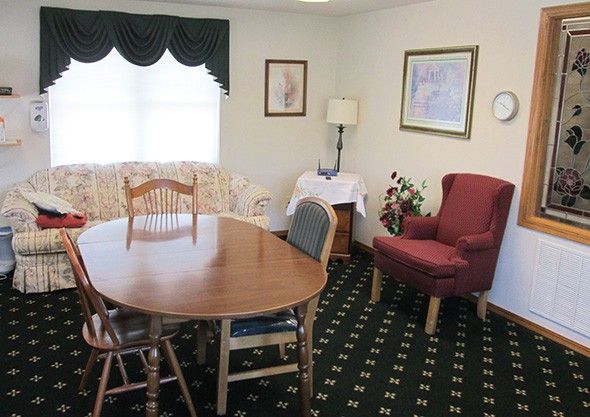 A cozy dining room with a wooden table, chairs, and an armchair, featuring artwork on the walls.