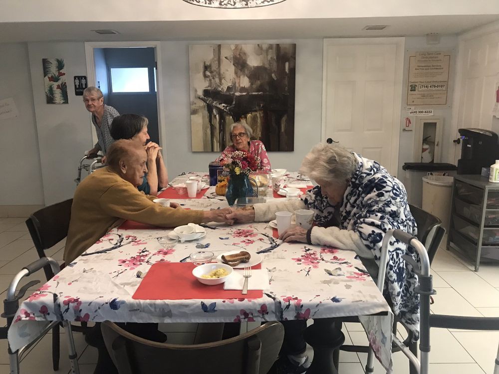 Elderly individuals enjoying a meal and engaging in conversation around a dining table.