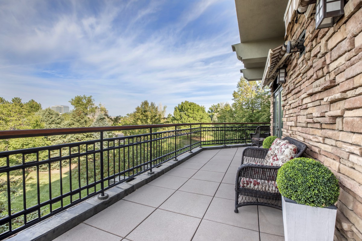 Spacious balcony with seating and a scenic view of trees under a clear sky.