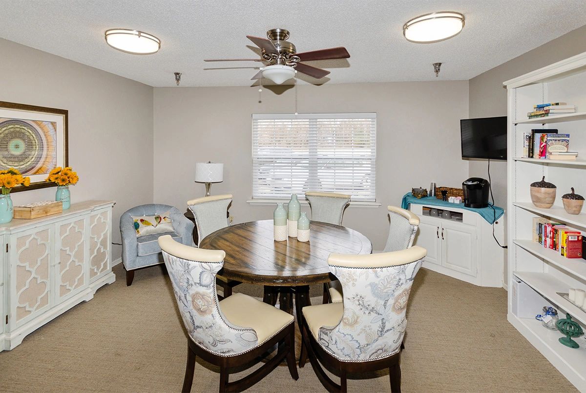 A cozy dining room with a round table and patterned chairs, complete with a ceiling fan and window view.
