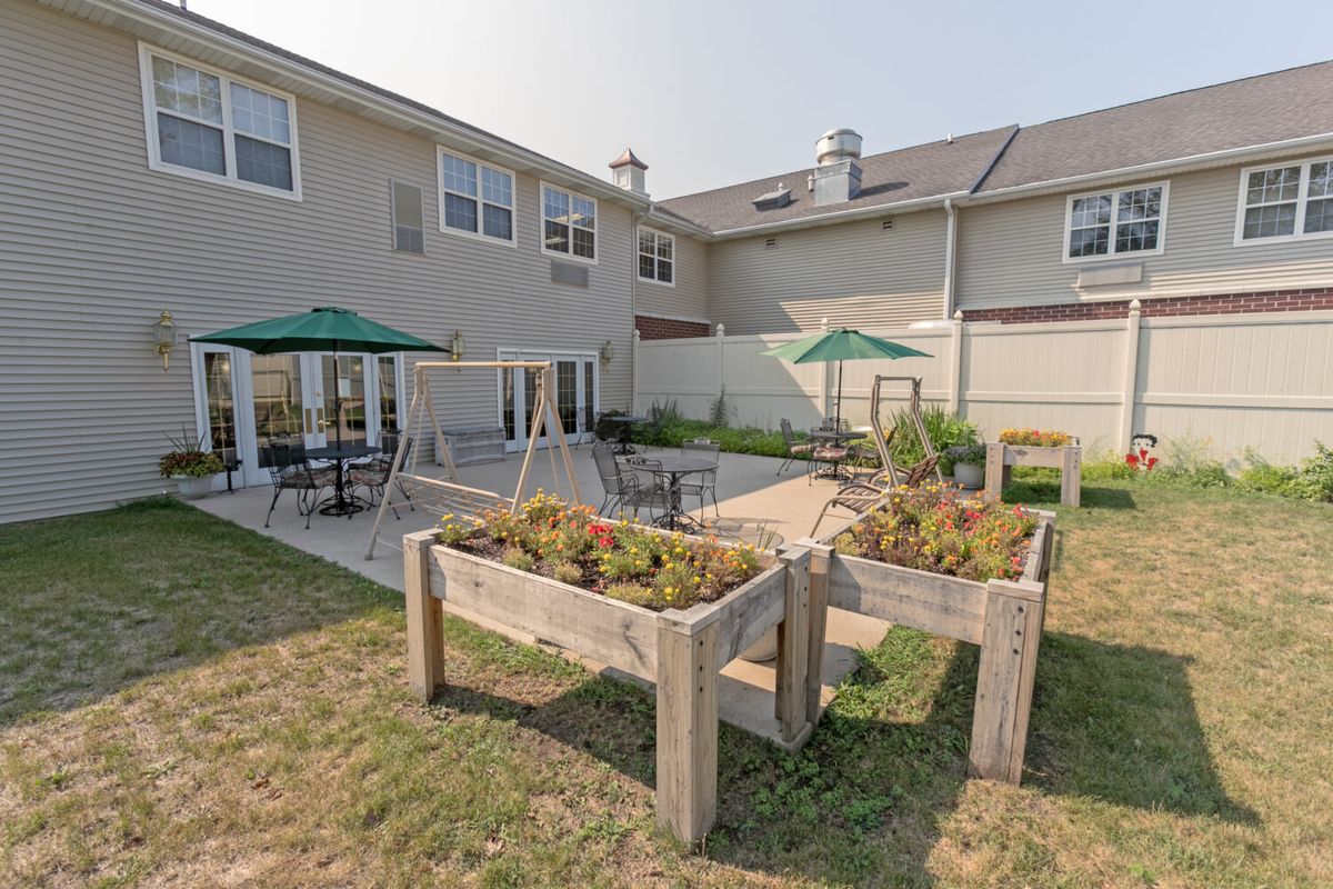 An outdoor patio area featuring tables, chairs with umbrellas, planters, and a two-story building in the background.