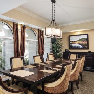 An elegant dining room with a large table surrounded by chairs, featuring a chandelier and artwork on the wall.