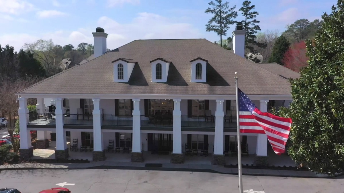 A large colonial-style building with prominent columns and an American flag in the foreground.