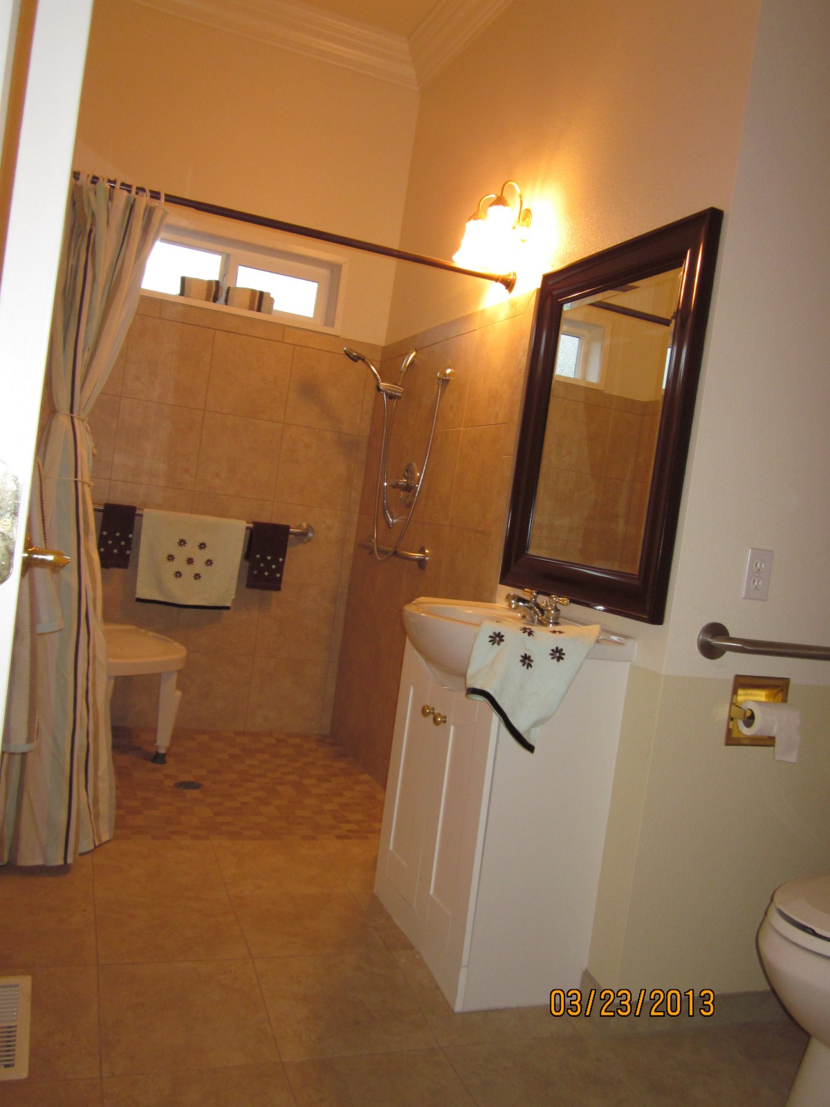 A well-lit bathroom featuring a sink with a mirror, shower area, and towels.