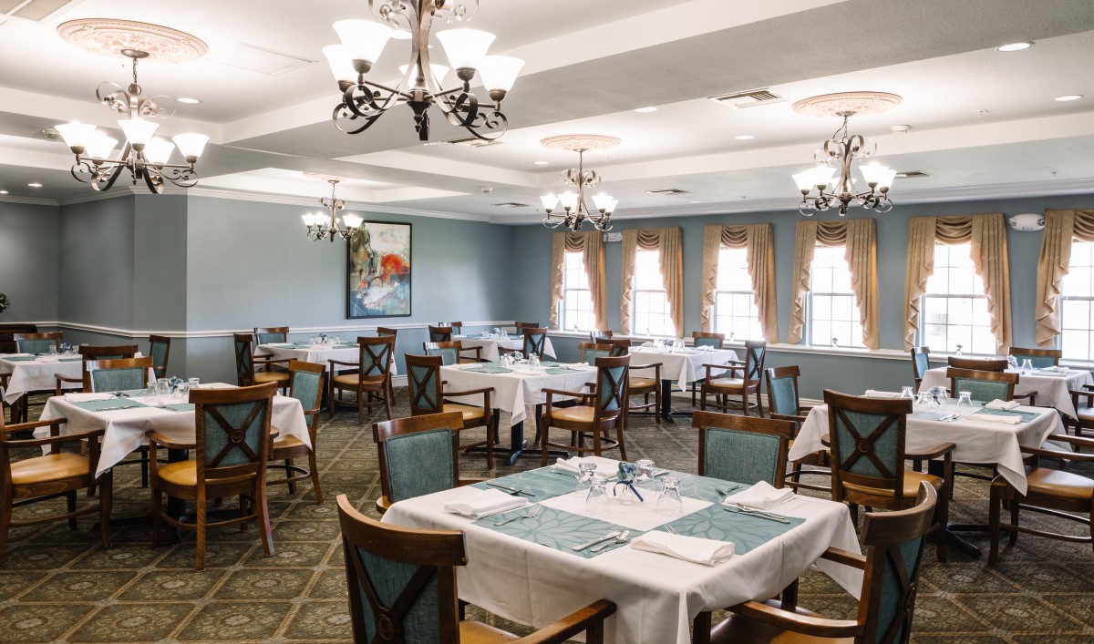 An elegant dining room with neatly arranged tables, white tablecloths, and chandeliers.