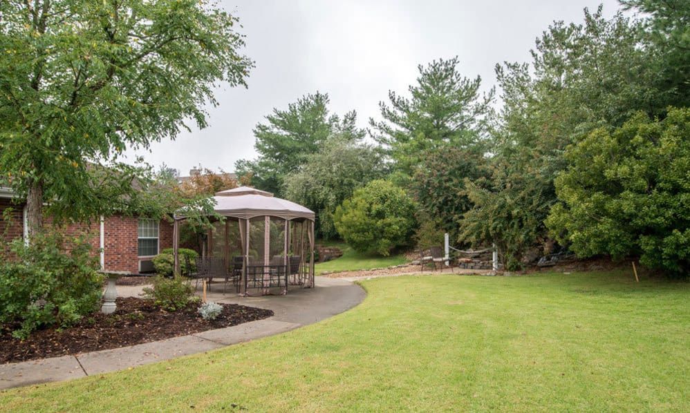 A peaceful garden scene featuring a gazebo, a manicured lawn, and lush trees.
