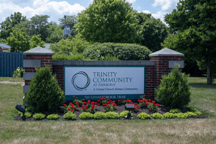 Entrance sign to Trinity Community surrounded by greenery and flowers.