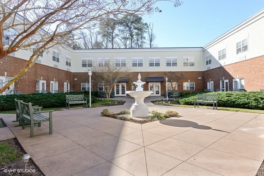 A courtyard featuring a central fountain surrounded by benches in front of a two-story building.