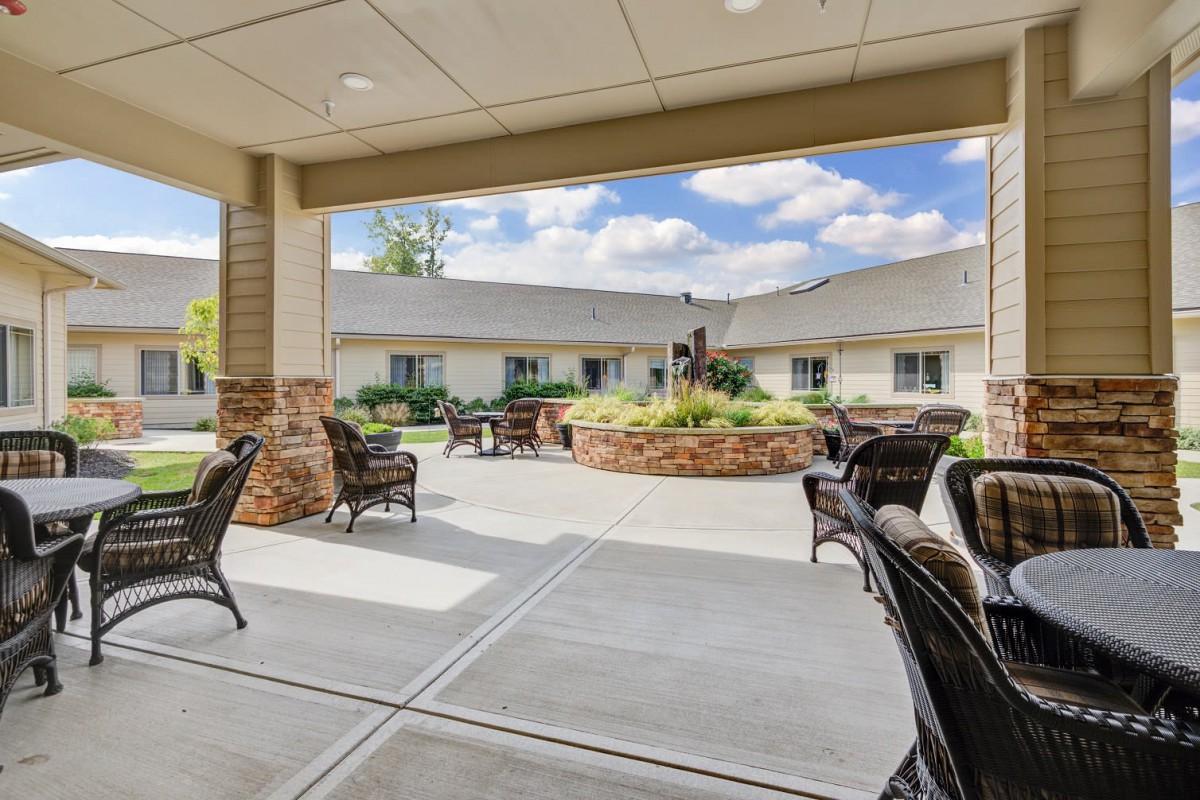 A view of an outdoor patio area with seating, situated in a landscaped courtyard beside a building on a cloudy day.