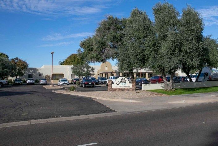 A commercial building surrounded by a parking lot with several cars and trees on a sunny day.