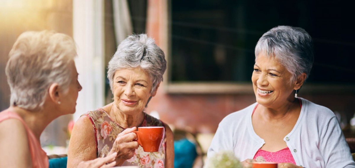 Two elderly women enjoying coffee and conversation outdoors.