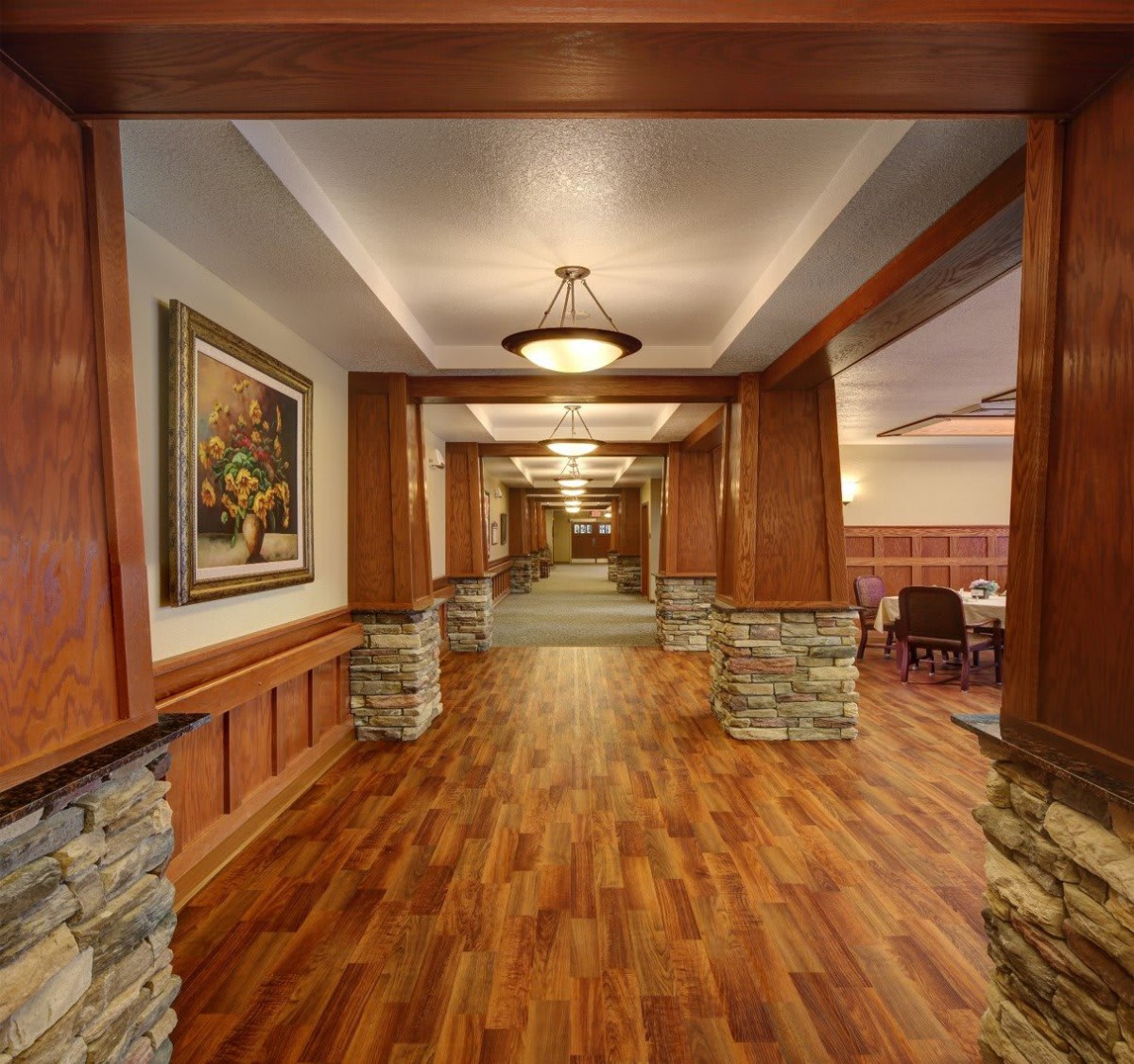 A warmly lit hallway with wooden floors and stone accents on the columns.