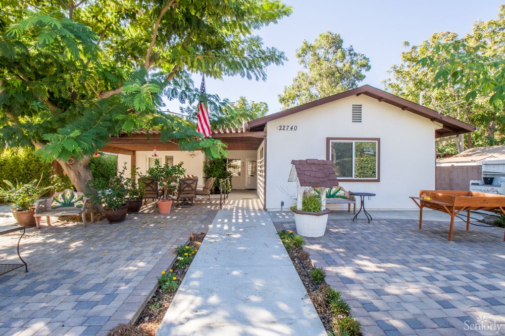 A charming residential house with a welcoming front yard, surrounded by trees and featuring a patio area.