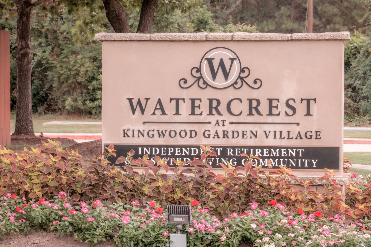 Entrance sign for Watercrest at Kingwood Garden Village, an independent retirement living community, with well-maintained landscaping and flowers.